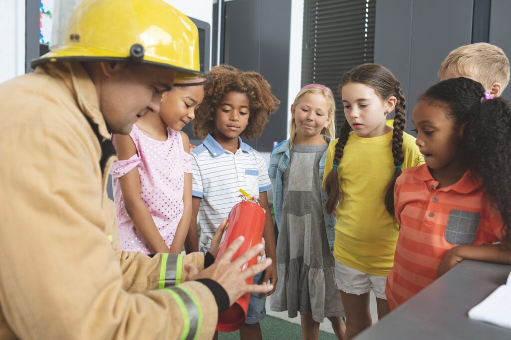 Firefighter teaching about fire extinguisher to school kids in classroom